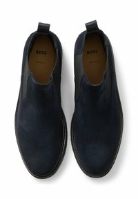 Zapatos náuticos de ante azul marino con paneles elásticos laterales y tira para tirar, con una textura suave y suela de goma negra. Marca visible en el interior.