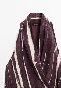 Tissu texturé rayé violet et blanc replié avec un col châle, montrant une étiquette Massimo Dutti à l'intérieur de l'encolure.