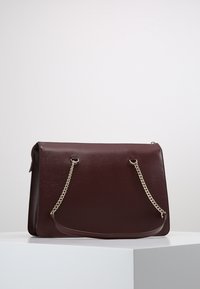 Burgundská kožená kabelka s hladkou texturou, stříbrnými řetízkovými detaily a plochým obdélníkovým tvarem. Má dvojité horní uchy pro nošení.