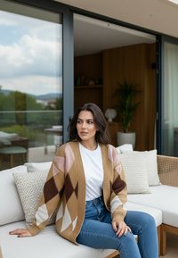 Kobieta w swetrze w wzory i białej koszuli siedzi na białej sofie na balkonie, w tle poduszki i zieleń.