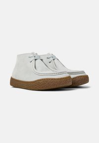 Zapatos de ante azul claro con una suela marrón texturizada, que presentan cordones sencillos y un diseño de tobillo bajo, exhibidos en un ángulo.