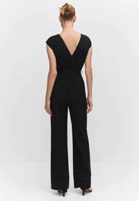 Mono negro con diseño de espalda en V, mangas cortas, cintura ajustada y pantalones de pierna ancha. El material parece suave con un ligero brillo.