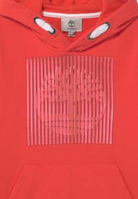 Felpa rossa con cappuccio, con spalline bianche, design trasparente a righe orizzontali sul davanti e tasca a marsupio frontale.