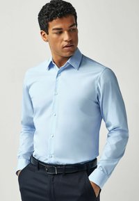 Himmelblaues Hemd mit spitzen Kragen, langen Ärmeln und Knopfleiste. Glatte Textur und slim fit Details.