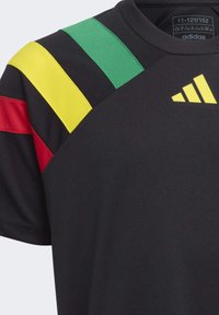 Schwarzes Sportshirt mit grünen, gelben und roten Streifen an der Schulter. Besitzt einen runden Halsausschnitt und das adidas-Logo in Gelb.