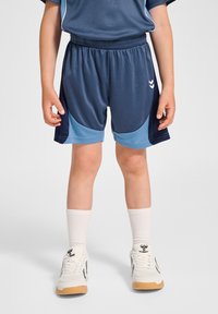 Marinblå sportshorts med ljusblå detaljer, elastisk midja och sidopaneler. Tillsammans med vita strumpor och sneakers.