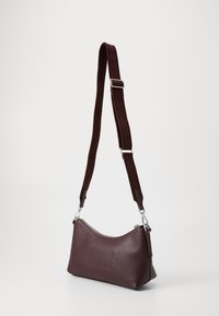 Sac à épaule en cuir bordeaux avec une finition texturée, doté d'une sangle détachable et de quincaillerie en argent, de forme courbée, avec une fermeture éclair.
