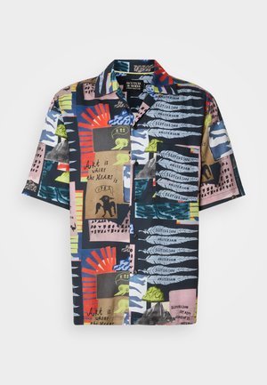 Camisa de manga corta con una base marina oscura y patrones abstractos vibrantes en rojo, verde, rosa y azul. El material parece ligero y colorido.