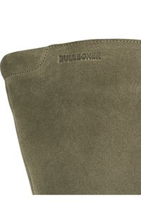 Oliveově zelený semišový kotník s zaobleným horním okrajem, embosované logo "BULLBOXER" a viditelné detaily šití. Celkově hladká textura.