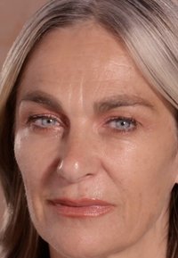Close-up van een gezicht met halflang, steil grijs haar. Kenmerken zijn onder andere lichtblauwe ogen, een gladde huid en subtiele make-up met een naakte lipkleur.