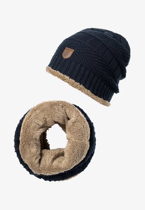 Dzianinowa granatowa czapka beanie z teksturowanym wzorem i beżowym futrem syntetycznym; pasujący okrągły szalik o podobnym kolorze i fakturze.