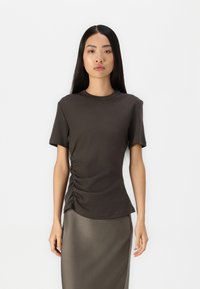 T-shirt fitted marrone scuro con maniche corte, dotato di un dettaglio arricciato sul lato. Tessuto di cotone liscio e elasticizzato. Collo rotondo semplice.
