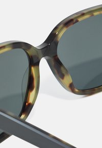 Ochelari de soare supradimensionați cu ramă din acetat cu model țestoasă, lentile întunecate și finisaj neted, lucios. Design unghiular cu temploare largi.