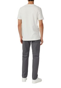 Witte katoenen t-shirt met korte mouwen, gecombineerd met grijze broek. Model draagt witte sneakers. Focus op basis-, casual ontwerp en kleuren.