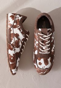 Braun-weiß gesprenkelte Sneaker aus Wildleder, mit rundem Zehenbereich, weißen Schnürsenkeln und einer strukturierten Gummisohle. Akzente setzen ein glattes seitliches Design.