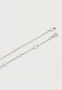 Δύο αλυσίδες από ασημί μέταλλο με μικρούς και μεγάλους κρίκους, η μία με κούμπωμα και στρογγυλή ταμπέλα με χαραγμένο το "DKNY".