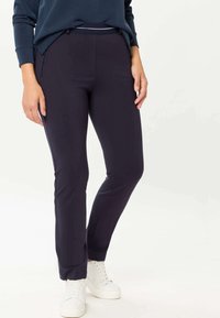 Navy stretchbroek met een slim fit en twee voorzakken, gecombineerd met witte sneakers. Glad textuur en een taps toelopend ontwerp.