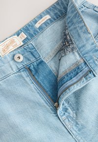 Jeans in denim blu chiaro con vestibilità rilassata, dotati di cerniera frontale, chiusura con bottone in metallo e fodera della cintura con motivo.