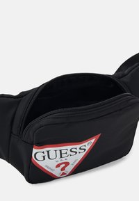 Černá nylonová pásek s kapsou na zip, s výrazným červeným a bílým trojúhelníkovým logem s nápisem "GUESS U.S.A.".