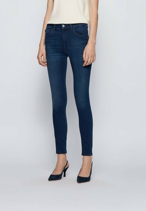 Slim-fit dark blue jeans worn with black slingback heels and a white sleeveless top, shown from mid-torso to feet against a plain background.