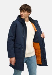 Námořnická parka s kapucí, která má prošívaný oranžový interiér, zapínací kapsy a přední patentky. Měkká tkanina s texturovaným povrchem.