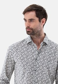 Weißes Hemd mit navyblauen Blumenmuster, mit Button-Down-Kragen, langen Ärmeln und glatter Textur. Besitzt dezente Blumen über den Stoff verteilt.