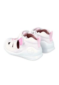 Zapatillas blancas para niños con acentos en rosa, que cuentan con una parte superior de tela suave, diseño abierto y correa de velcro. Suela de goma texturizada.