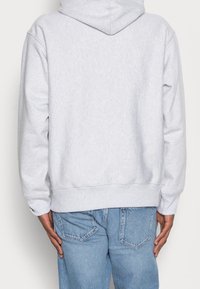Světlě šedá mikina s kapucí a texturovaným povrchem. Navržena s volnějším střihem a žebrovanými manžetami, doplněná modrými džínami.