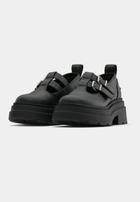 Fekete platform cipő sima bőrből, két állítható pánttal és ezüst csattal díszítve. Négyzet alakú orr és texturált gumitalp.