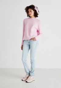 Lichtroze geribbelde trui met ronde hals, gecombineerd met lichtblauwe slim-fit jeans en pastel sneakers met zwart-witte accenten.