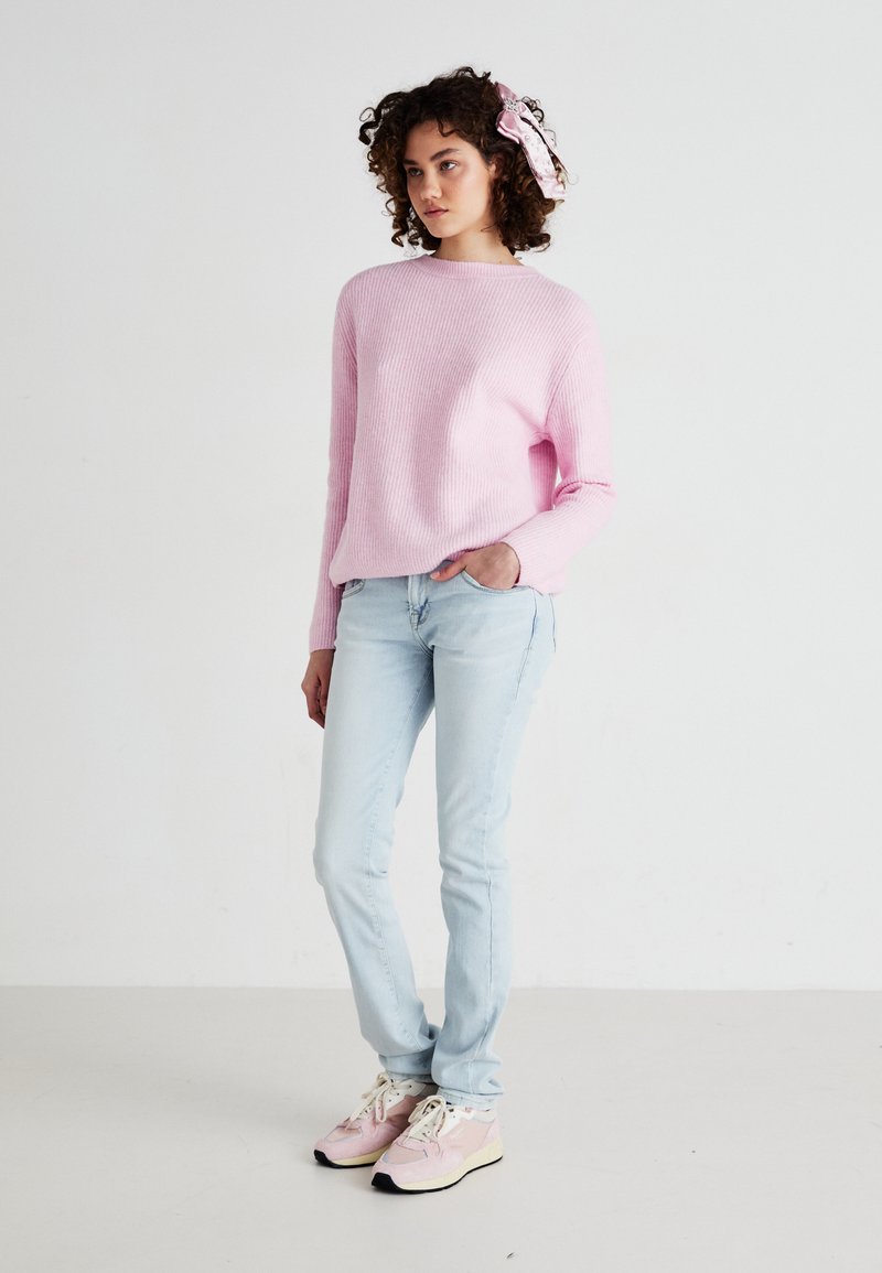Lichtroze geribbelde trui met ronde hals, gecombineerd met lichtblauwe slim-fit jeans en pastel sneakers met zwart-witte accenten.