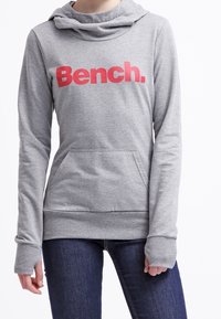 Felpa grigia a maniche lunghe con collo a cowl e tasca frontale. Presenta un audace logo rosso "Bench.", polsini a coste e un taglio rilassato.