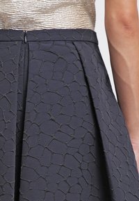 Grå kjol med strukturerat rutmönster och veck. Tyget är vävt och har en subtil lyster vid midjan. Dragkedjestängning bak.