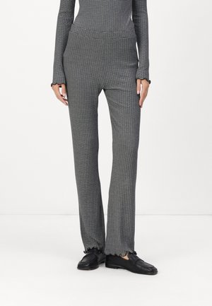 Grå ribbede bukser med vertikale striper, med en tettsittende midje, utsvingte buksebein og bølget kant, kombinert med svarte slip-on sko.