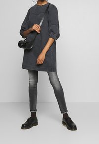 Svart denimklänning med puffärmar och sydda detaljer, i kombination med gråa slim fit-jeans och svarta snörskor. Liten svart axelremsväska.