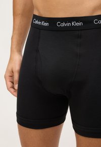 Boxer briefs de algodón negro con una cinturilla suave que presenta el logo en blanco de "Calvin Klein". Textura suave, diseño ajustado y longitud a mitad del muslo.