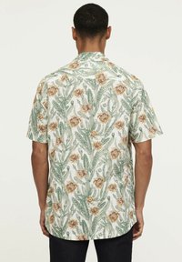 Korte mouwen, geknoopte blouse gemaakt van lichte stof, met een bloemen- en cactuspatroon in groen, beige en roomkleur.