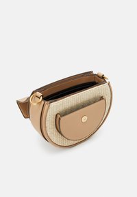 Borsa a tracolla in pelle color cuoio con fronte intrecciato in paglia, forma circolare, ferrature dorate e una tasca a patta. La parte superiore aperta rivela un interno nero.