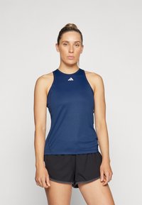 Marineblauwe mouwloze sporttop van gladde stof, met een slim fit en logodetail bij de halslijn, gecombineerd met zwarte shorts.