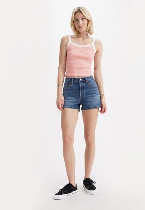 Randig orange linne med vita axelremmar, parat med högmidjade blå jeansshorts. Modellen bär svarta sneakers med vita sulor.