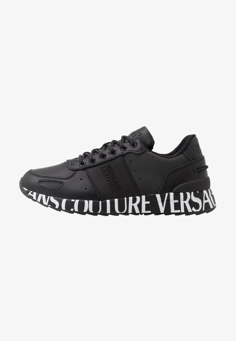 Baskets noires en matériau lisse, avec une semelle blanche épaisse arborant un audacieux marquage "VERSACE COUTURE" et des lacets sur le dessus.