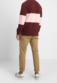 Bordeauxrood en roze gestreepte trui, kaki taps toelopende broek, opgerolde broekspijpen en grijze sneakers. Casual outfit van achteren gezien.