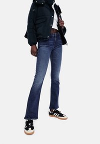 Mörkblå utsvängda jeans kombinerat med en svart puffjacka, vit topp och svart-vita sneakers med gummisula.