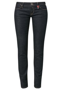Jeans de mezclilla azul oscuro con ajuste slim, con costuras en contraste, cierre frontal de botón y un pequeño detalle del logo rojo en la cintura.