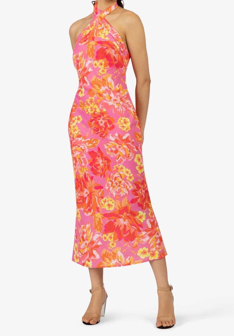 Robe à bretelles nouées au cou à motifs floraux roses, ornée de fleurs orange vif et jaunes. Coupe mi-longue avec un corsage ajusté et une jupe évasée.