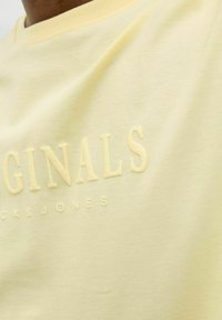 Žluté bavlněné tričko s texturovaným logem 'ORIGINALS' a názvem značky 'Jack & Jones' v světlých barvách, s klasickým crew neck designem.