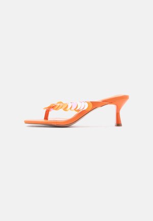 Narancssárga magassarkú szandál talpbetét pánttal és díszítő kör alakú flitterekkel a felsőrészén, egyszerű fehér háttér előtt.