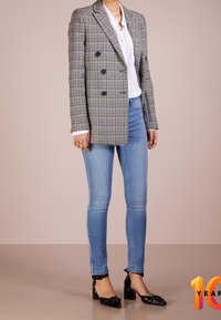 Dubbelt knäppt rutigt kavaj i grått, svart och blått, matchat med ljusblå skinny jeans och svarta lackpumps med rosettdetaljer.