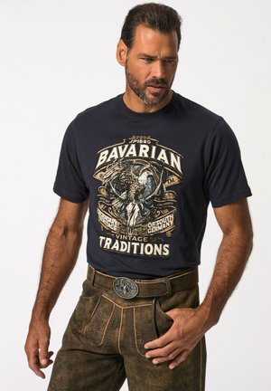 Marineblå grafisk t-shirt med et centralt ørnedesign og tekst, parret med brune strukturerede bukser med bælte og udsmykket spænde.