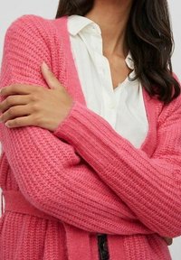 Růžový pletený kardigan s dlouhými rukávy, texturovanou látkou a páskem v pase. Nosit přes bílou košili na knoflíky, ukazující volný střih.